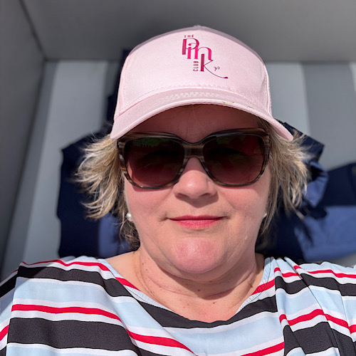 img 2025 05 17 152327 Birgit Nora Schäfer mit Sonnenbrille und rosa Cap lächelnd im Strandkorb